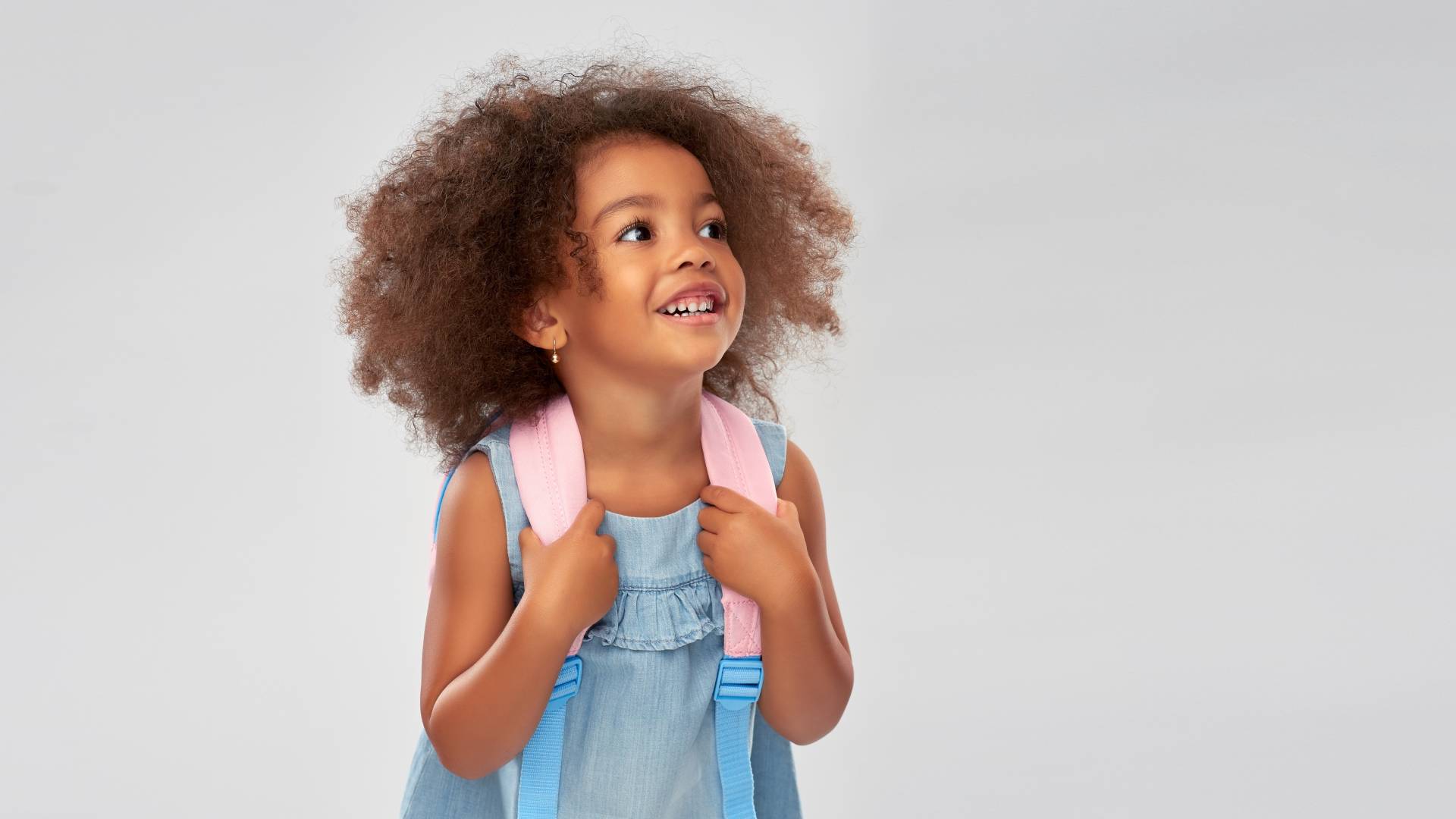 AdobeStock_296840914 a young girl standing and holding her backpack
