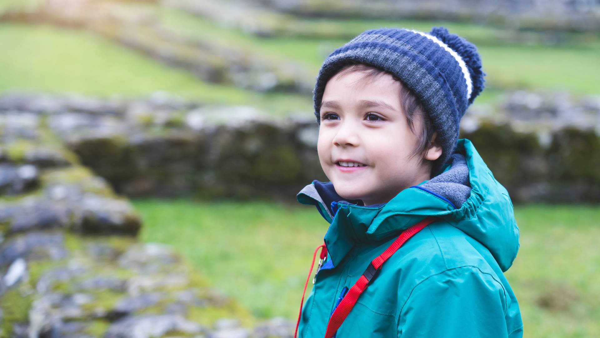 AdobeStock_345299531 a child in a blue wooly hat and a green coat standing outside