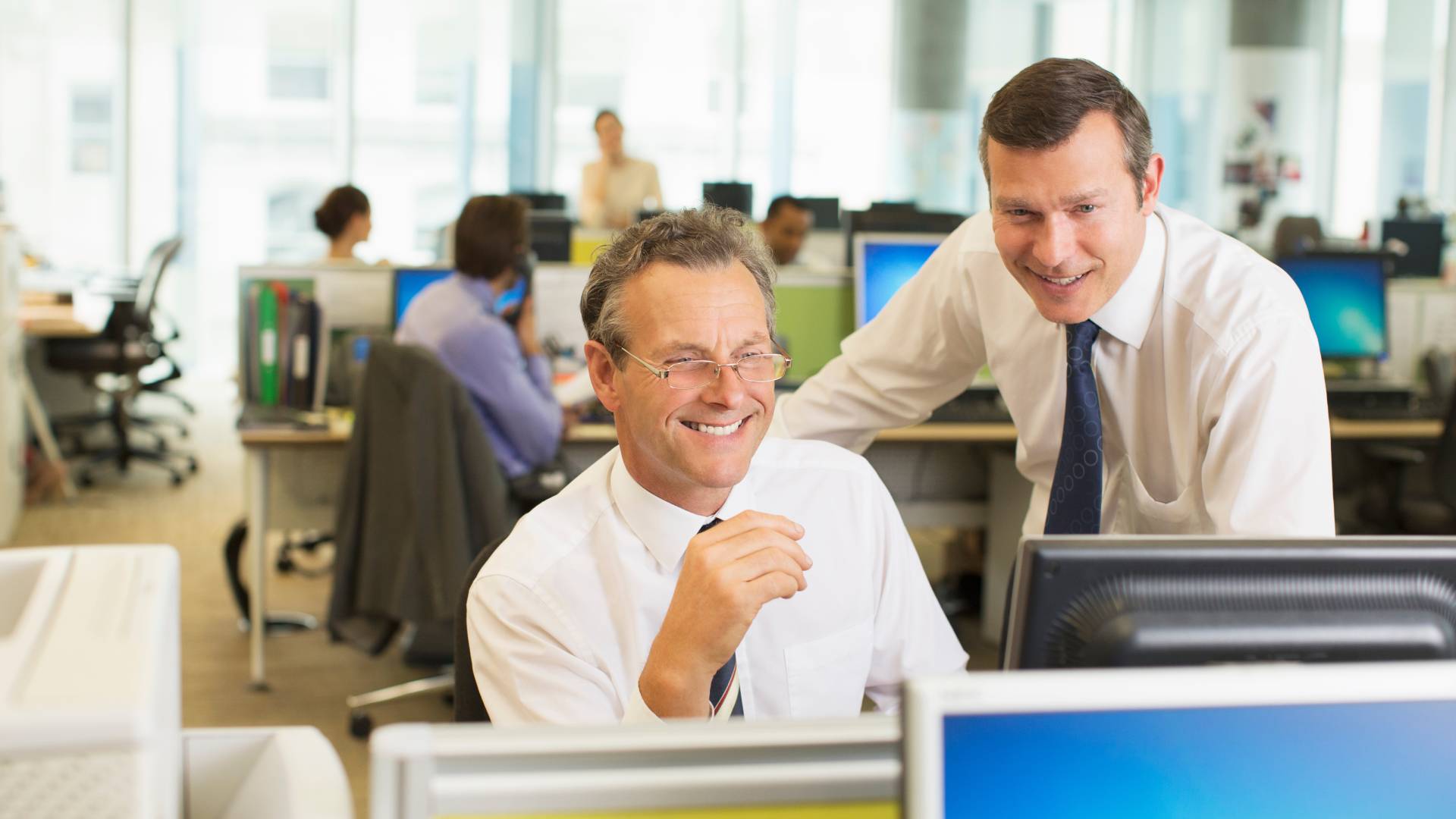 AdobeStock_357285961 2 men in white shirts and ties standing smiling in the office in front of a their computer