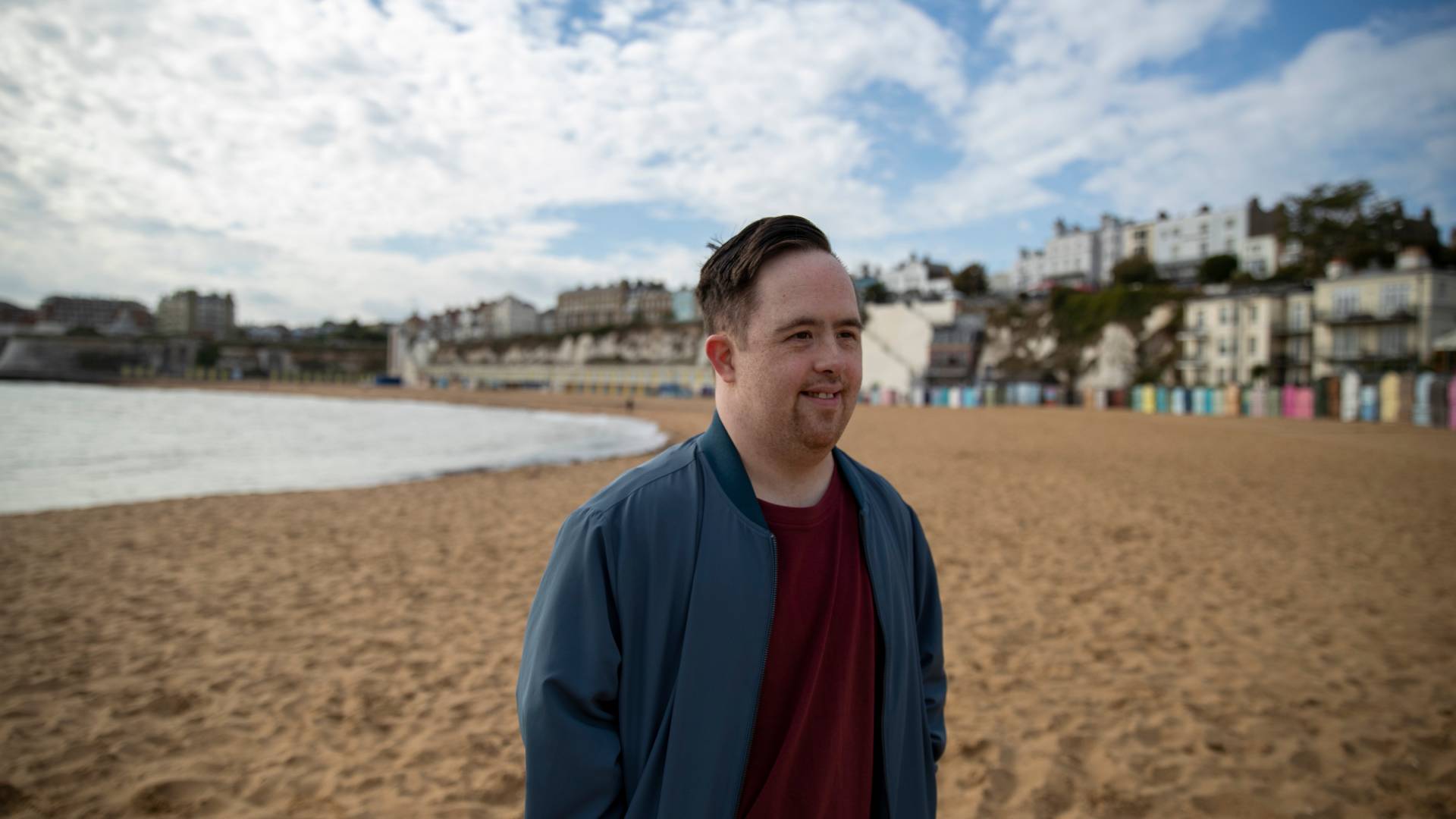 AdobeStock_544858337 a man at the beach with buildings behind him