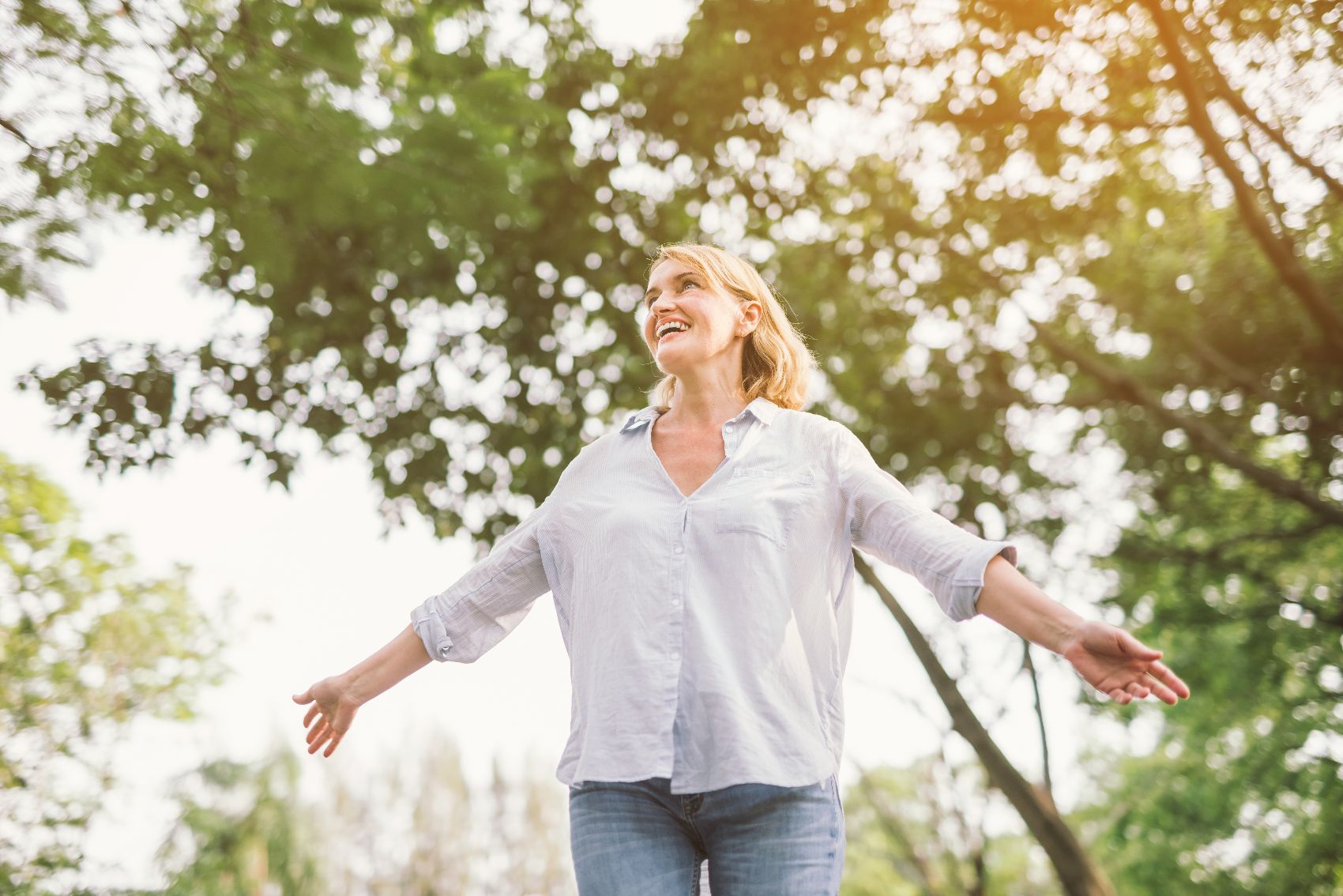 Anxiety 1 a woman in a white shirt standing in the sunlight with her arms spread out and smiling