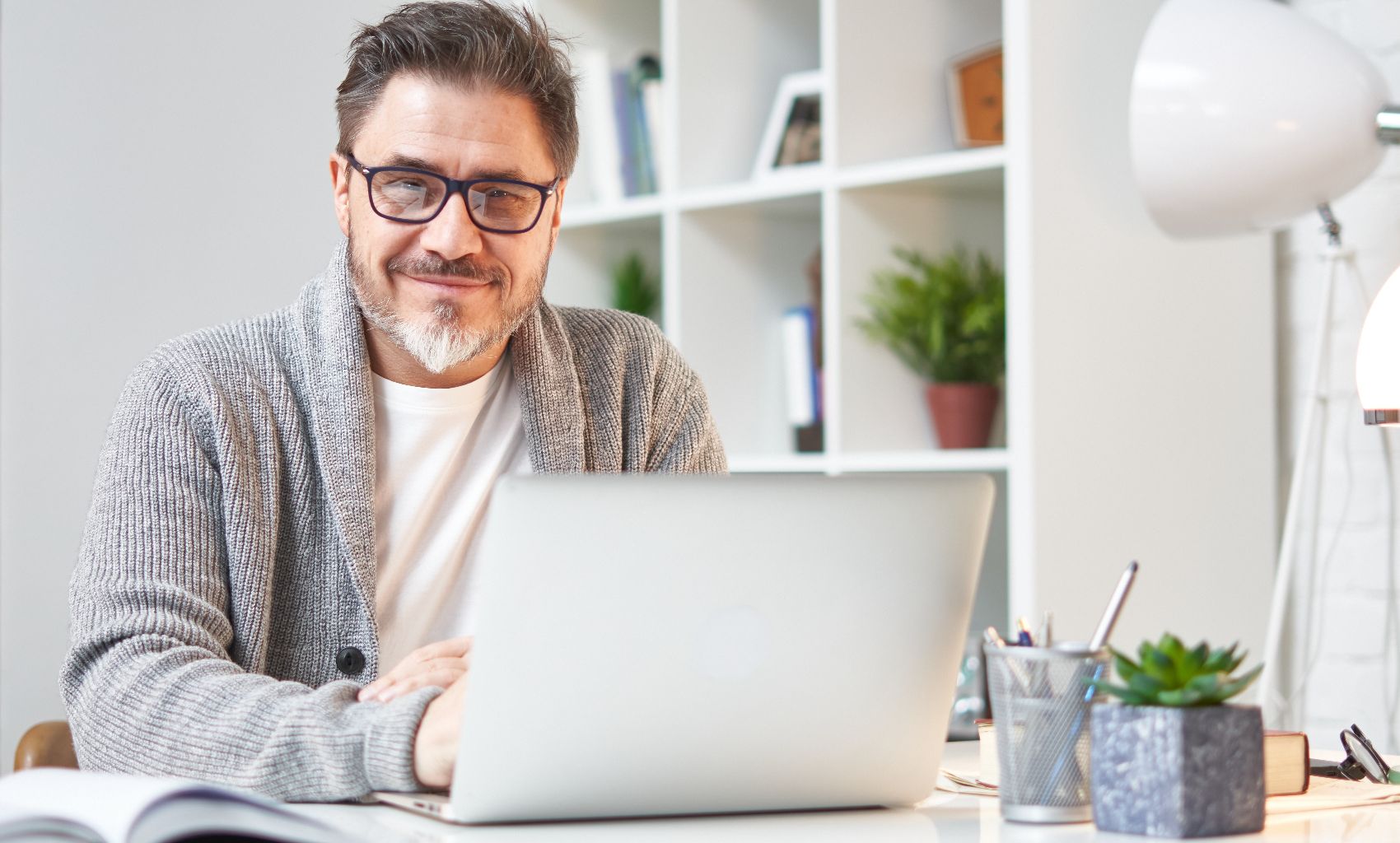 Image 14 a man in a grey cardigan and glasses on his laptop smiling at the camera