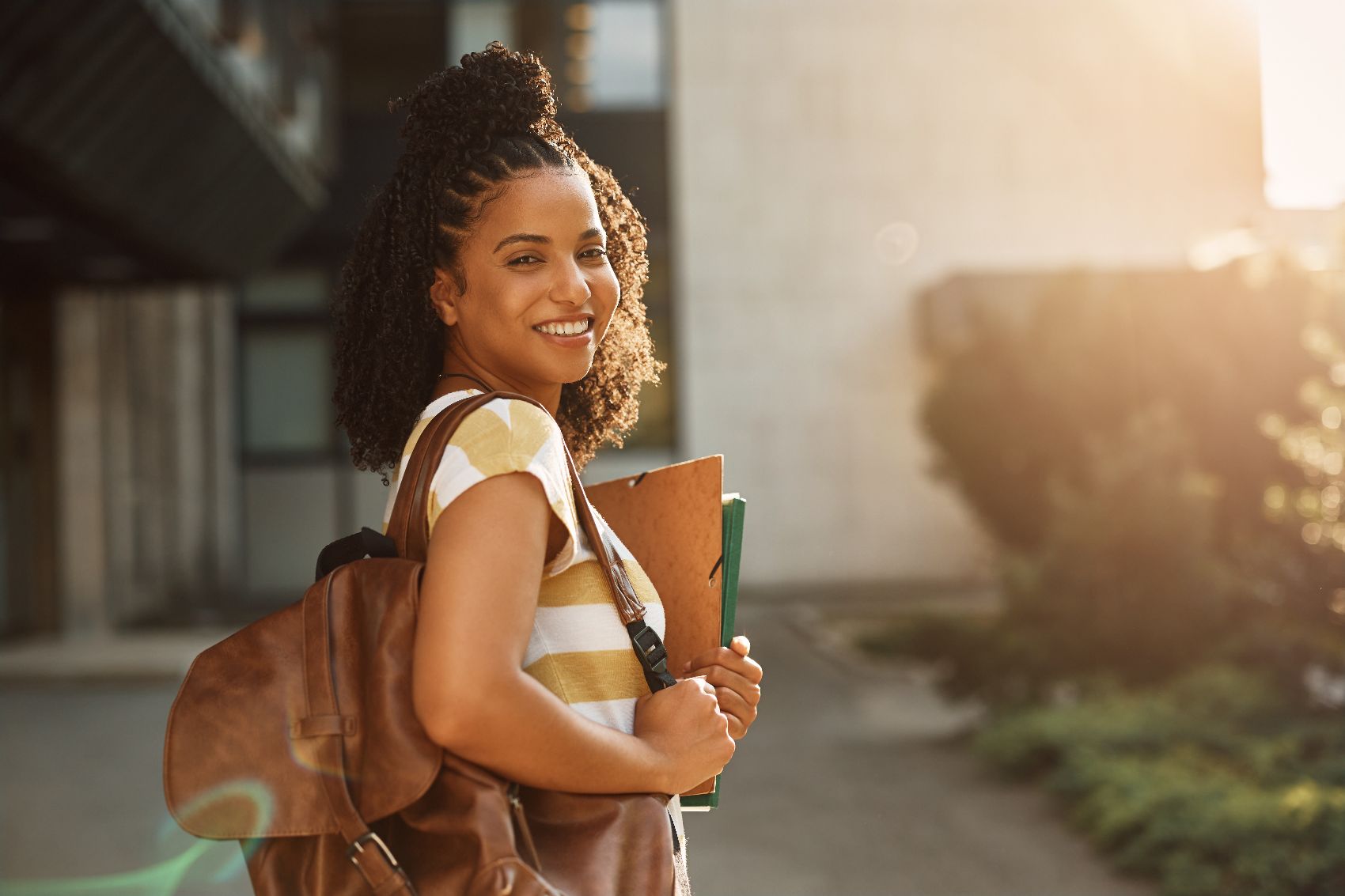 Image 8 a woman outside holding a notebook and a folder smiling at the camera