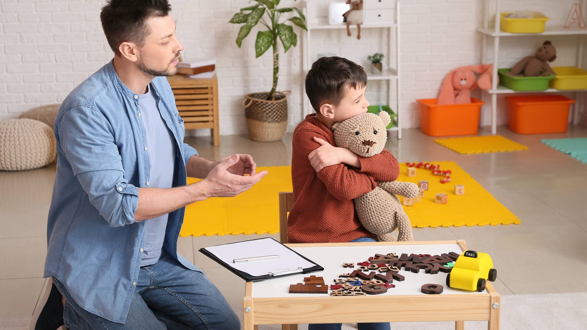 Subtypes of autism a man holding a teddy bear with his back turned while a male therapist tries too interact with him