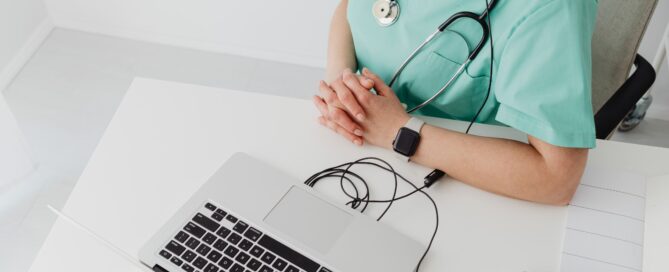 Doctor in green scrubs sitting in front of a laptop